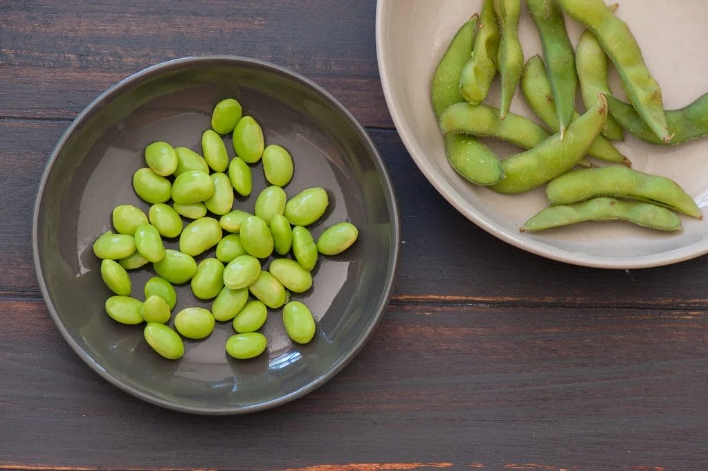 edamame in a plate next to a plate containing edamame beans